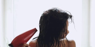 深色头发的女人用毛巾在家里用吹风机烘干头发