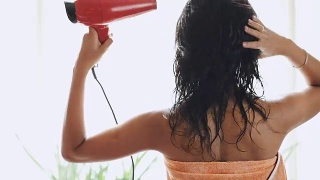 深色头发的女人在家里用电吹风吹头发，后视图视频素材模板下载