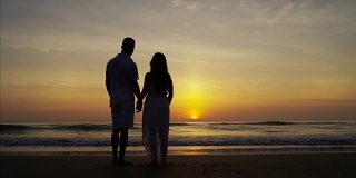 年轻的西班牙夫妇享受海滩日出的剪影