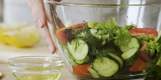 女士将新鲜的沙拉拌上橄榄油，然后在碗里搅拌，这是健康的饮食
