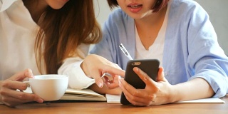 商务女性使用手机，在木桌上写报告。用手机和咖啡的亚洲女性。在咖啡店工作的自由职业者。在外工作的生活方式。
