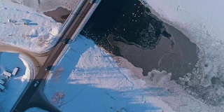 寒冷的冬天。从上面俯瞰，可以看到冰封的河流上的桥，在开阔的水面上有一大群鸭子和天鹅。无人机视频与静态摄像机。