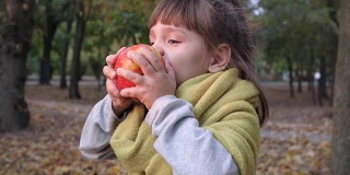 可爱的小女孩吃苹果的背景上的黄色树叶在秋天的自然特写