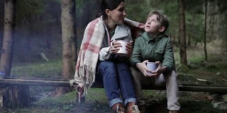 母亲和儿子坐在包裹在格子的篝火前，喝着茶