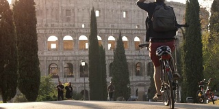 一名年轻游客独自骑着自行车在罗马竞技场前的路与树木日落慢镜头
