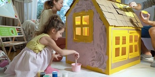 年轻的家庭和孩子一起建造和油漆玩具纸板房子