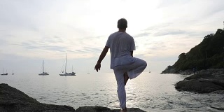男子在海岸的石板上表演瑜伽动作