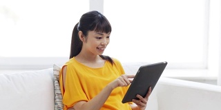 快乐的年轻亚洲女人在家里有平板电脑