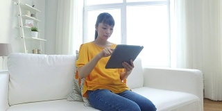 快乐的年轻亚洲女人在家里有平板电脑