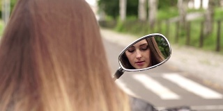 女孩对着摩托车镜子画了她的嘴唇。