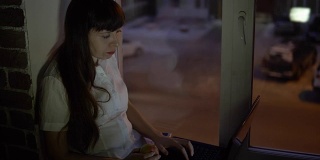 一位女商人坐在靠近一扇暗窗的窗台上，用笔记本电脑工作。