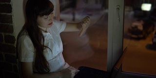一位女商人坐在黑窗边的窗台上，用笔记本电脑工作