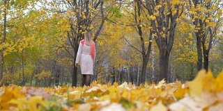 米色大衣和橙色围巾的女士走在秋天的黄叶地毯4k