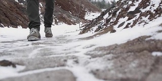 男性的腿在冬天的鞋子走在雪地上的特写。镜头，在冬天穿着雪鞋和钉鞋在雪地上行走的景象。穿靴子的男人们的腿挡住了白雪覆盖的小路