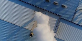 烟从工厂或工厂的屋顶上的管道排出，生产车间的屋顶上有一根管道，白色的浓烟从管道排出