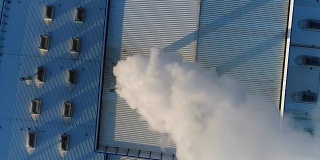 烟从工厂或工厂的屋顶上的管道排出，生产车间的屋顶上有一根管道，白色的浓烟从管道排出