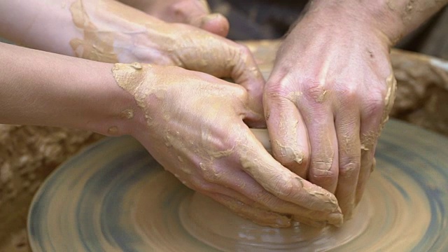 两只手交织在一起，在陶工转盘上形成一个陶罐。