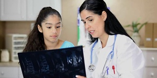 拉丁女医生拿着病人的x光片。她正在给年轻的拉丁女病人做体育检查。
