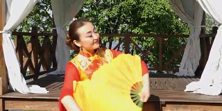 美丽的亚洲女人穿着红色的传统中国服装和两个大的黄色扇子跳舞。