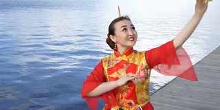 美丽的中国女孩穿着传统的红色中国服装和大的黄色扇子在河边