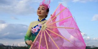 美丽的中国女孩穿着中国传统服装，拿着大粉扇在河岸上跳舞