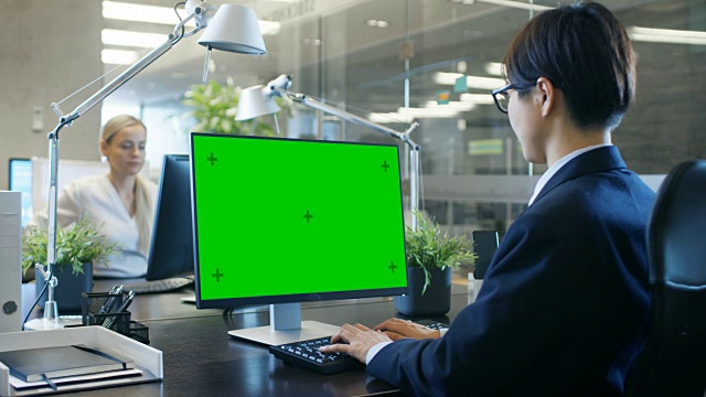 在办公室里，商人在他的办公桌上用一台模拟的绿色屏幕的个人电脑工作。同事走进办公室，并在她的办公桌前发生。