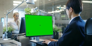在办公室里，商人在他的办公桌上用一台模拟的绿色屏幕的个人电脑工作。同事走进办公室，并在她的办公桌前发生。