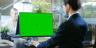 在办公室里，东亚商人在一台模拟绿色屏幕的台式个人电脑上工作。他戏剧性地转头，越过肩膀看向镜头。同事走进办公室，并在她的办公桌前发生。