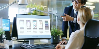 在办公室里，女设计师坐在她的办公桌前与她的经理谈话，她的个人电脑显示了她设计的新手机应用程序的UI设计。时尚的设置。