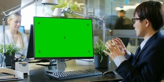 在办公室，商人在模拟绿色屏幕的个人电脑上进行视频通话。他与接受者交谈并积极地做手势。