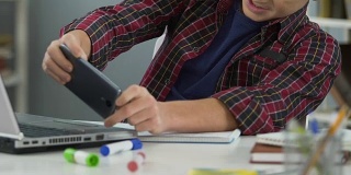懒惰的男性青少年在智能手机上玩手机游戏，而不是做作业