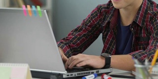 十几岁的男孩微笑着在笔记本电脑上打字，做作业，学生工作