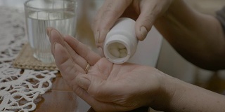 一个年长的女人的手正在清空她掌中的药瓶并吞下了所有的药丸