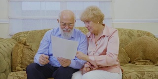一对老年夫妇坐在客厅的沙发上查看房租账单