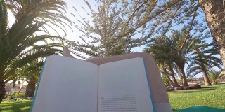 一名男子正在热带花园的日光浴床上看4K慢镜头的书
