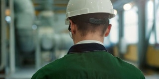 带安全帽的工程师在工厂里行走并在剪贴板上写字的背影