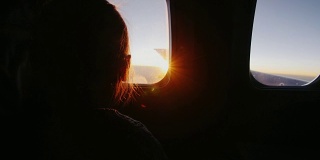 小女孩坐在飞机上，高兴地看着窗外冉冉升起的太阳
