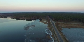 4 k编译视频。在早春日落时飞过结冰的湖面上的公路，鸟瞰图