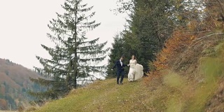 一对年轻美丽的新婚夫妇一起从山上跑下来。结婚的那一天。慢动作