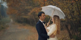 一对年轻美丽的新人一起站在秋林前的白色伞下。结婚的那一天。慢动作
