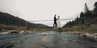新郎新娘在河上的桥上相会。一对年轻美丽的新婚夫妇。结婚的那一天。慢动作