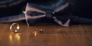 结婚戒指在蓝色新郎领结前的地板上滚动