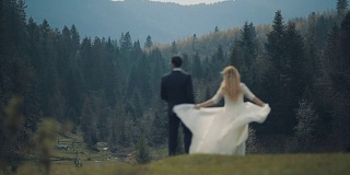 一对年轻美丽的新婚夫妇一起站在山坡上，看着美丽的山林景色。慢动作