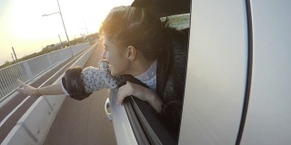 快乐迷人的女人在夕阳西下时，在汽车的后座上愉快地挥手，她的头伸出窗外