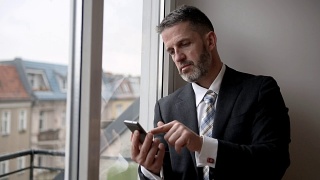 一个商人站在窗边用手机写字的画面视频素材模板下载