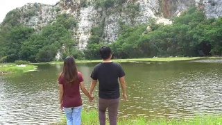 Man and woman or couple walk together holding hands in nature with mountain and river. Happy freedom and travel concept.视频素材模板下载
