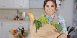 微笑的女人在厨房里拿着一袋购物用品
