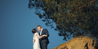 一对年轻美丽的新婚夫妇站在山坡上接吻。结婚的那一天。慢动作