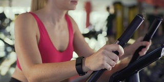 运动女孩骑健身自行车和监测距离的健身手环
