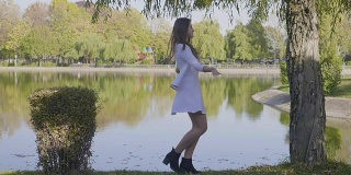 慢镜头中，一个美丽的年轻女孩穿着白色衣服，长发飘飘地在公园的湖边旋转
